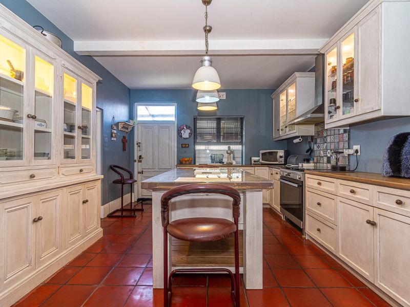 A well-appointed kitchen featuring classic white cabinetry, a central island, tiled flooring, and integrated appliances with stylish glass-fronted display units.