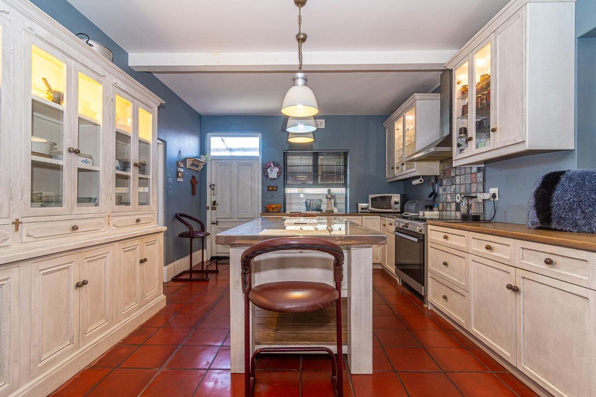 A well-appointed kitchen featuring classic white cabinetry, a central island, tiled flooring, and integrated appliances with stylish glass-fronted display units.