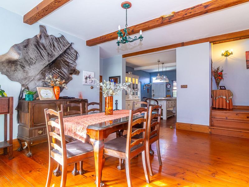 Dining room featuring exposed timber ceiling beams and polished hardwood flooring, with an open-plan transition into the adjacent kitchen area.