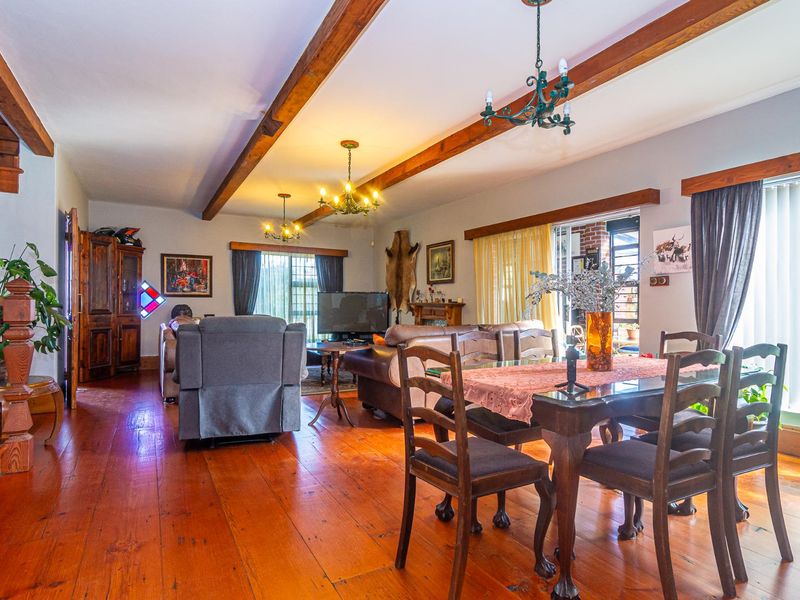 Spacious open-plan living and dining area featuring warm timber flooring, exposed ceiling beams, and a classic timber staircase.