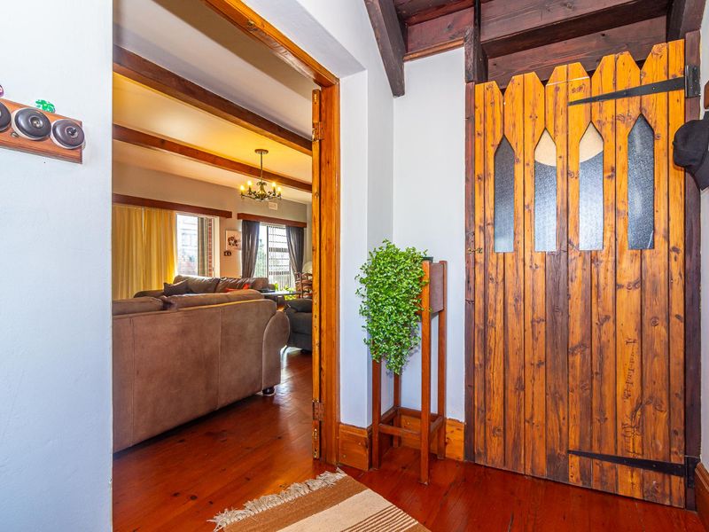 A rustic-style hallway featuring warm timber flooring, exposed ceiling beams, and a distinctive wooden door with glass detailing, leading into the main living area.