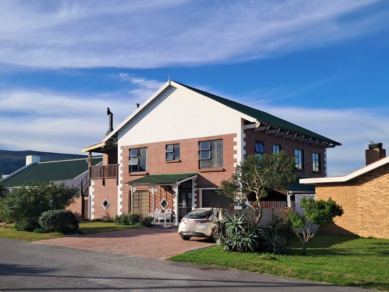 A two-story brick house featuring a pitched roof, paved driveway, and an attached balcony, set within a well-maintained residential neighborhood.