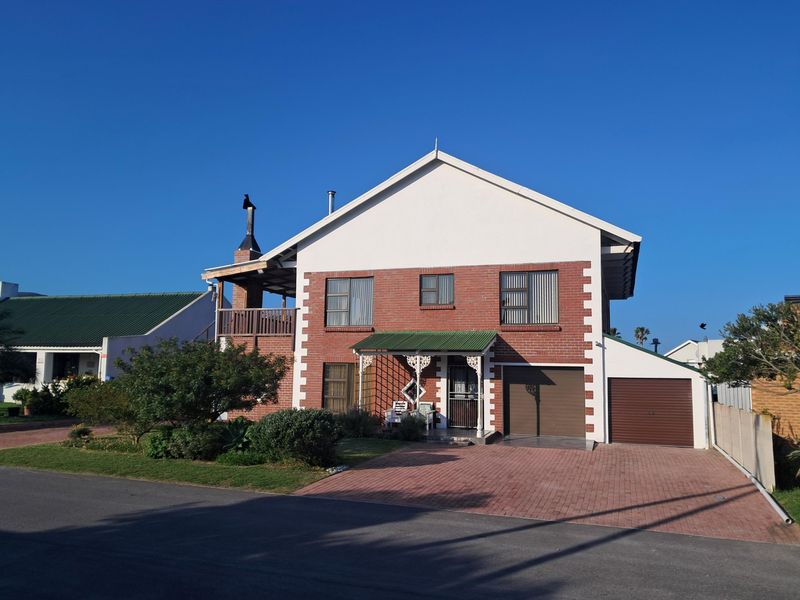 A two-story brick house featuring a double garage, paved driveway, and an upper-level balcony with a chimney.