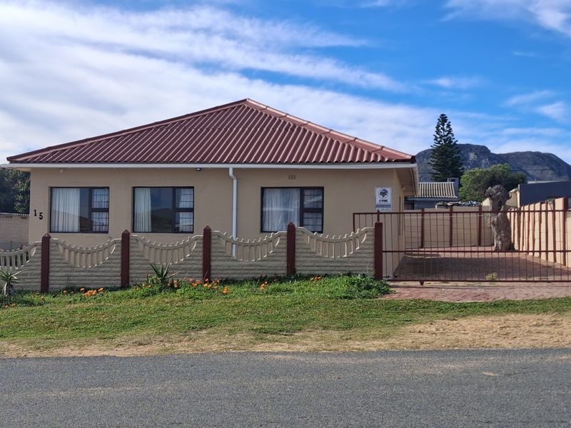 Front elevation of a single-story house featuring a corrugated metal roof, paved driveway, and secure perimeter fencing.