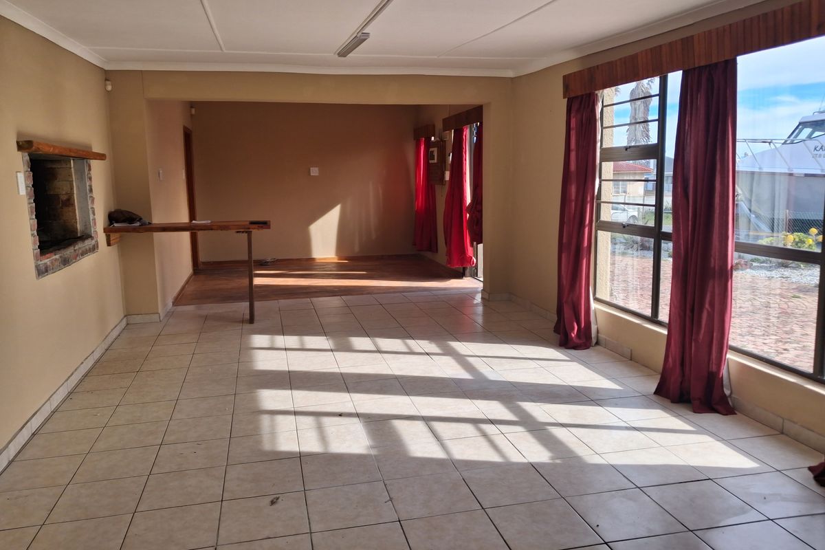 Spacious, empty living area featuring tiled flooring, a built-in indoor braai, and large windows allowing for ample natural light.