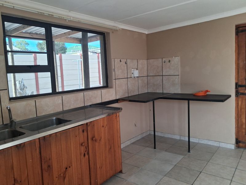 A functional kitchen area featuring a stainless steel sink, tiled splashback, and wooden base cabinetry, offering a blank canvas for potential renovation.