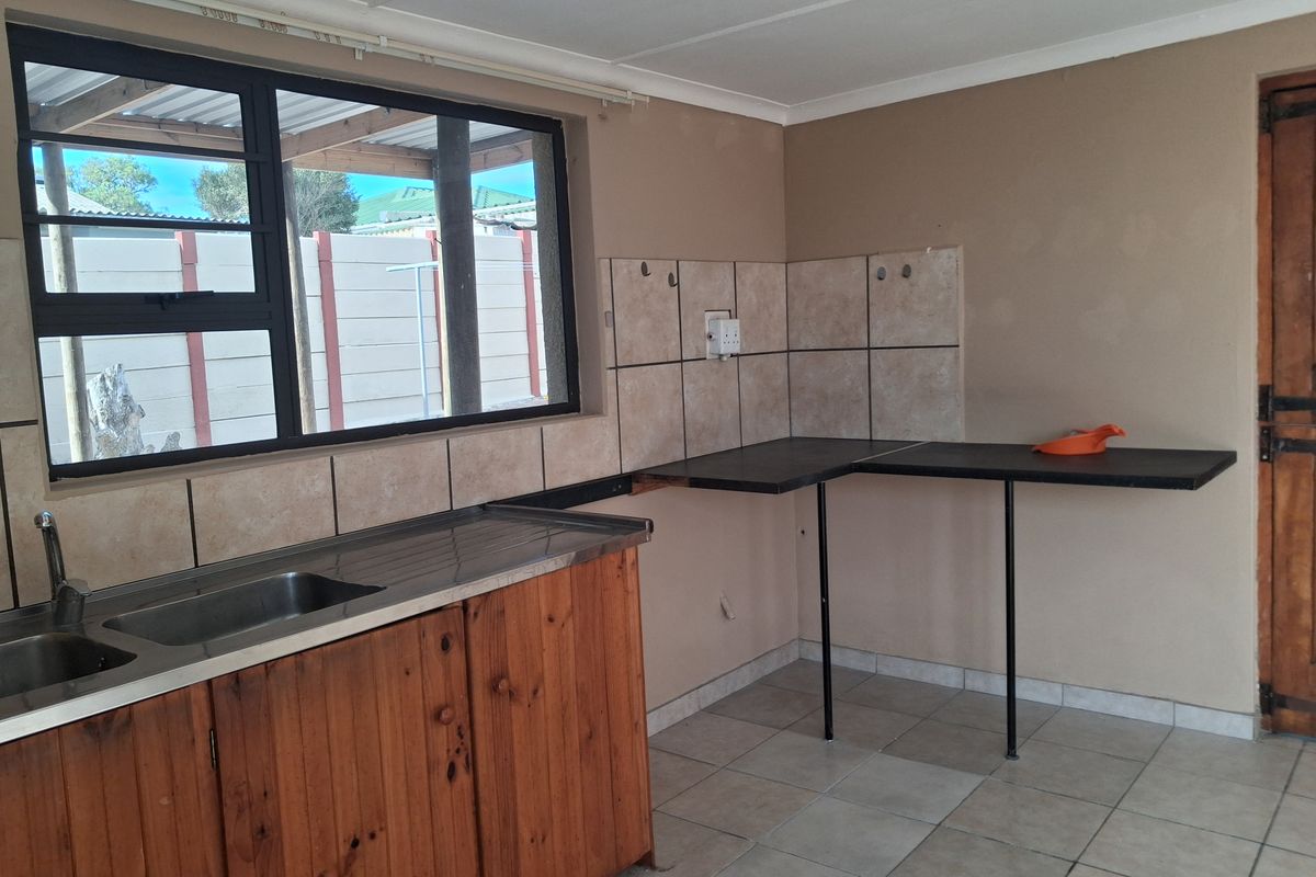 A functional kitchen area featuring a stainless steel sink, tiled splashback, and wooden base cabinetry, offering a blank canvas for potential renovation.
