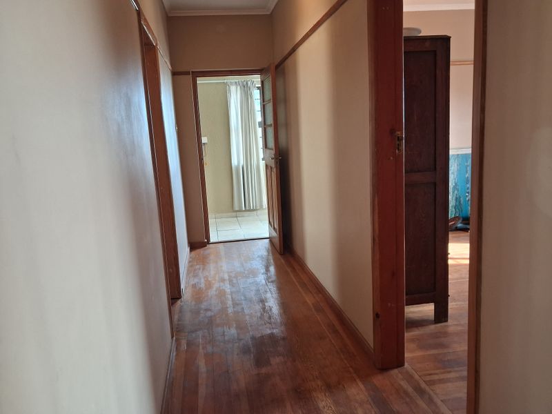 A narrow hallway featuring original timber flooring and wooden door frames, leading to adjacent rooms and an exterior doorway.