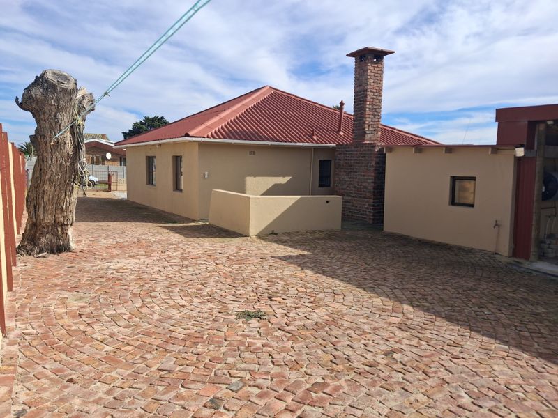 Rear exterior view of the property featuring a brick chimney, corrugated metal roof, and extensive cobblestone paving in the courtyard area.