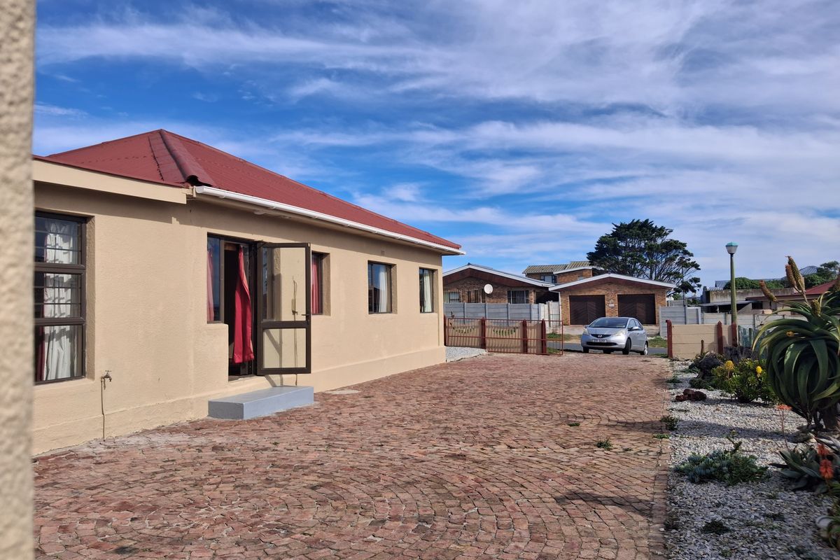 Rear view of the property featuring a brick-paved driveway, metal roof, and secure boundary walling in a well-maintained outdoor space.