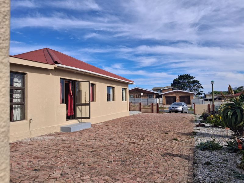 Rear view of the property featuring a brick-paved driveway, metal roof, and secure boundary walling in a well-maintained outdoor space.