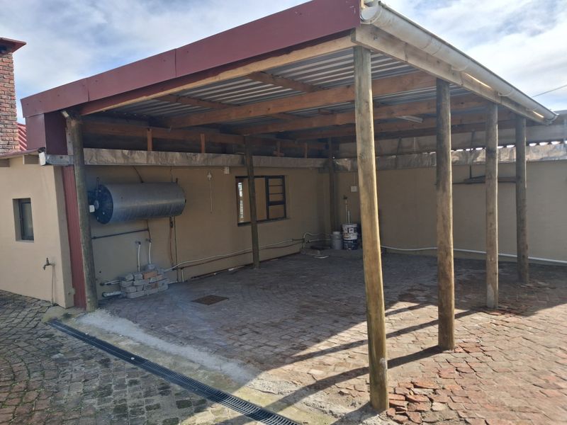 A covered outdoor patio area featuring timber support posts, brick paving, and an external geyser, offering potential for a functional outdoor entertainment space.