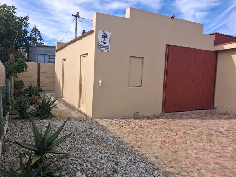A detached garage structure featuring a brick-paved driveway and secure metal doors, situated within a fenced property with low-maintenance landscaping.