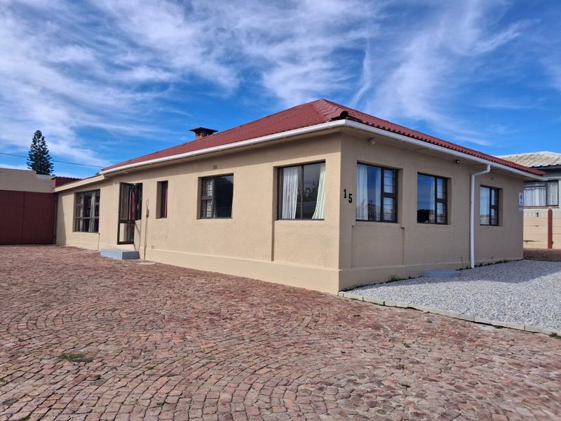 A well-maintained single-story house featuring a red metal roof, plastered exterior walls, and a spacious brick-paved driveway.
