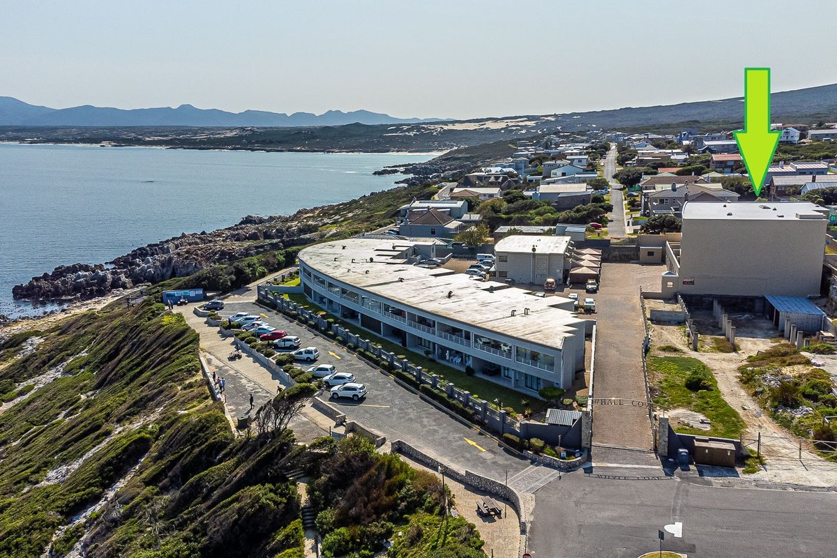 Aerial view of the apartment complex situated along the coastline, featuring dedicated parking areas and proximity to the ocean.