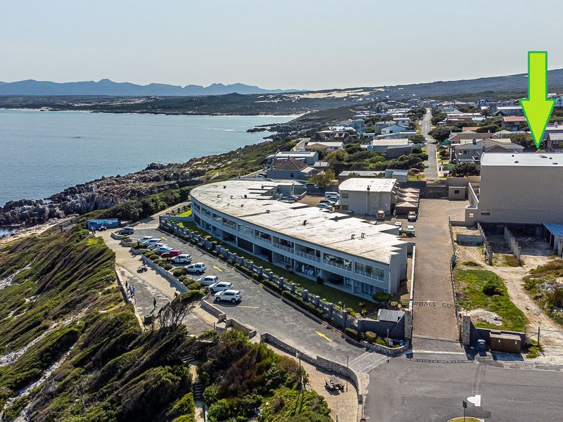 Aerial view of the apartment complex situated along the coastline, featuring dedicated parking areas and proximity to the ocean.