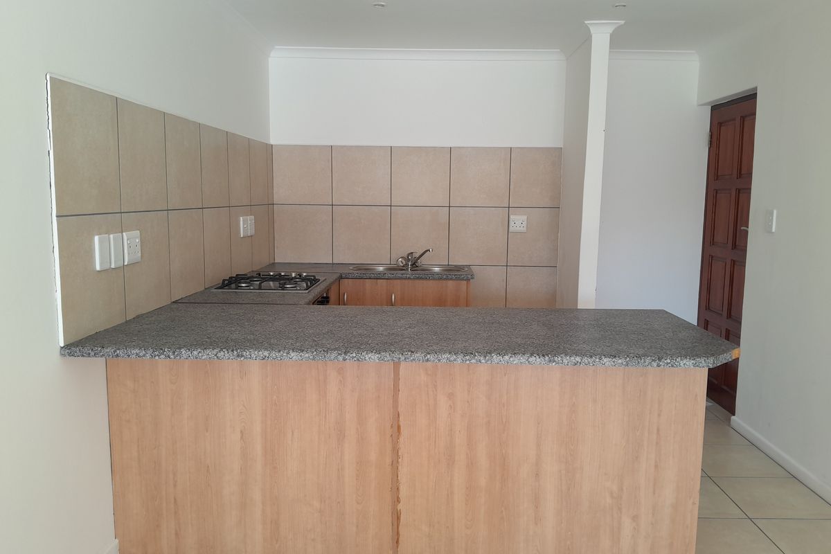 A functional kitchen featuring light wood cabinetry, granite countertops, a gas hob, and a double sink with neutral tiled splashbacks.