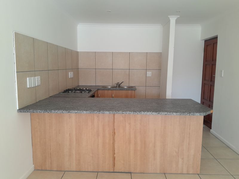 A functional kitchen featuring light wood cabinetry, granite countertops, a gas hob, and a double sink with neutral tiled splashbacks.