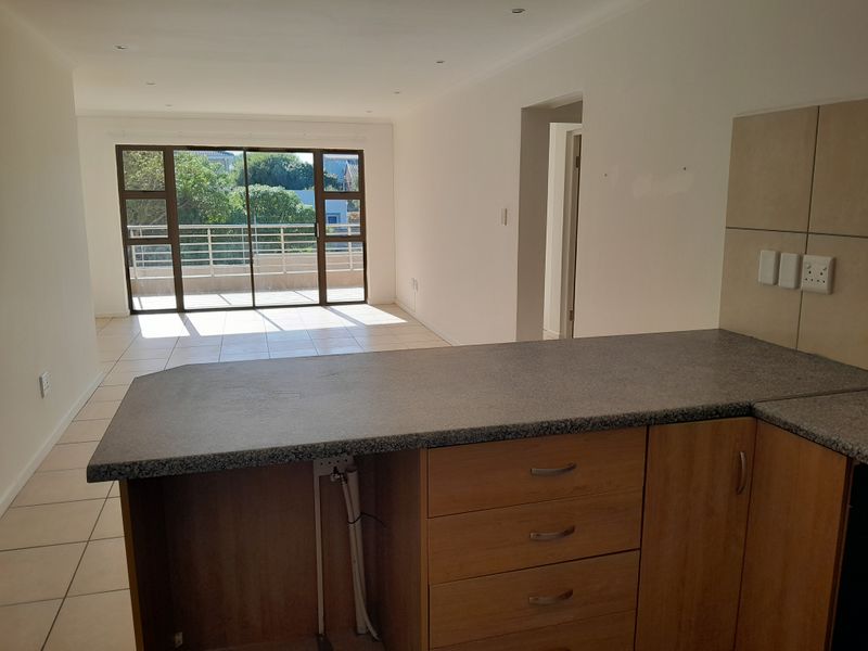 An open-plan living area featuring tiled floors, a kitchen with built-in cabinetry and granite countertops, leading to a balcony through sliding glass doors.