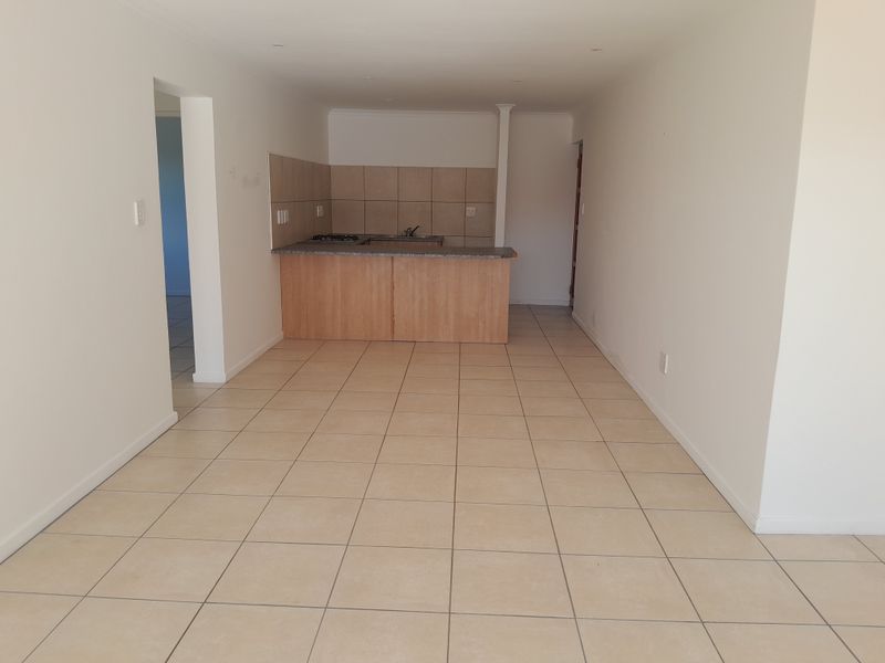 An open-plan living and kitchen area featuring neutral tiled flooring, built-in cabinetry with granite countertops, and a functional kitchen layout.