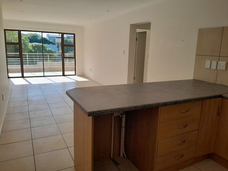 Spacious open-plan living area featuring tiled floors, a kitchen island with cabinetry, and large sliding doors leading to a private balcony.