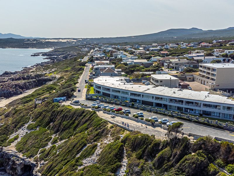 Aerial view of a coastal apartment complex situated on a cliffside, featuring paved parking and proximity to the ocean and local coastline.