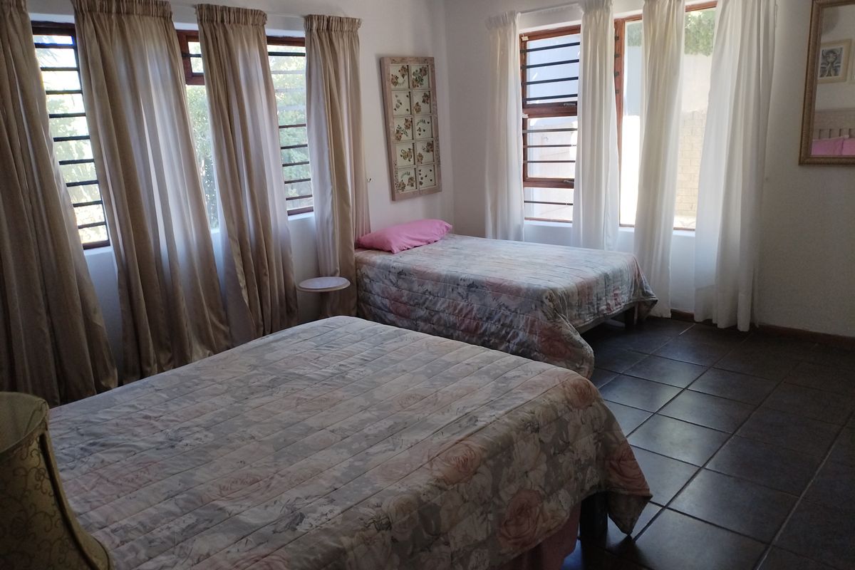 A spacious bedroom featuring tiled flooring and large windows with security bars, offering natural light and a functional layout.