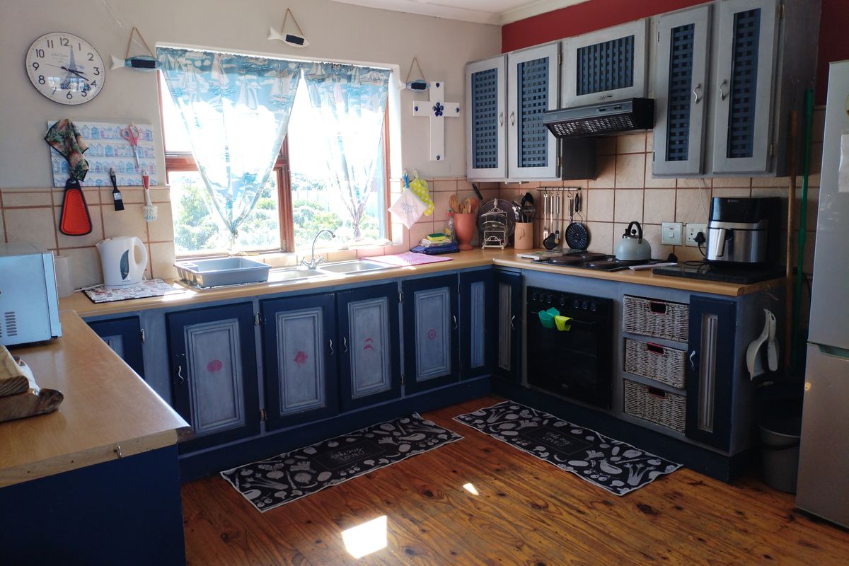 A functional kitchen featuring timber flooring, built-in cabinetry, a double sink, and integrated cooking appliances with a tiled backsplash.