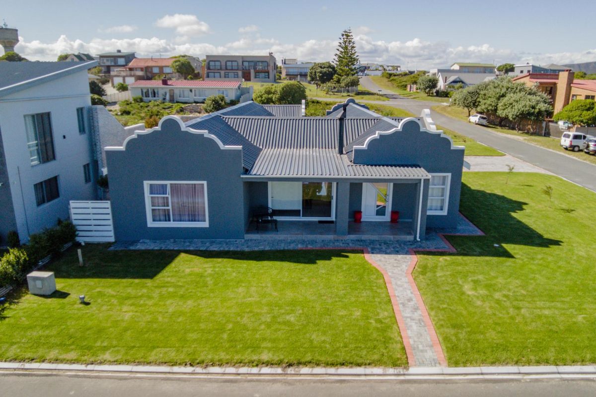 Aerial view of a well-maintained single-story house featuring a grey facade, corrugated metal roof, and a neat front lawn with a paved walkway.