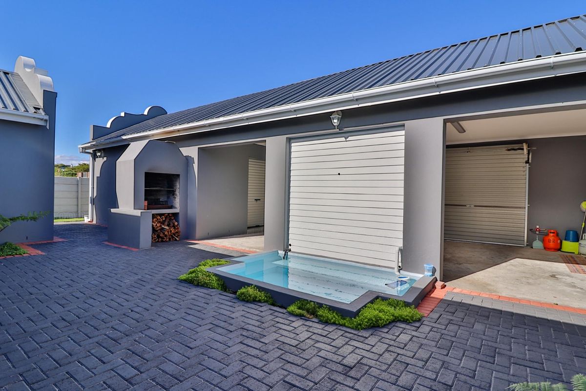 Rear courtyard featuring a paved patio, built-in braai area, and a small plunge pool, adjacent to the garage access.