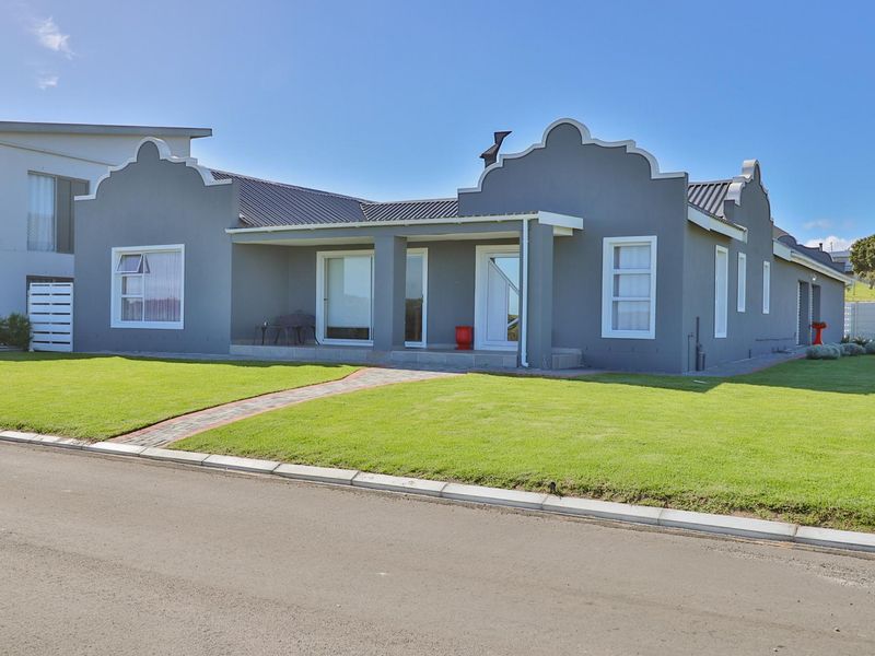 A well-maintained single-story house featuring a grey facade, covered front patio, paved walkway, and a neat lawn.