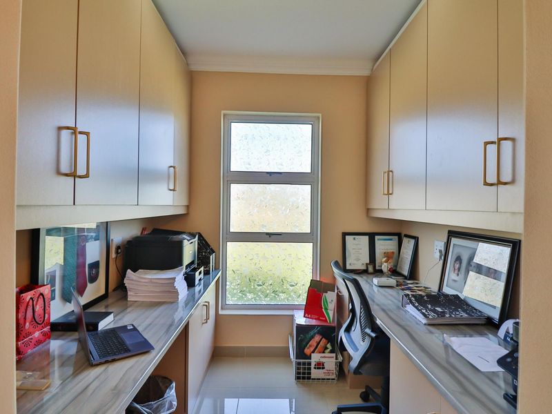 A functional home office featuring extensive built-in cabinetry, laminate work surfaces, and a window with frosted glass for privacy.
