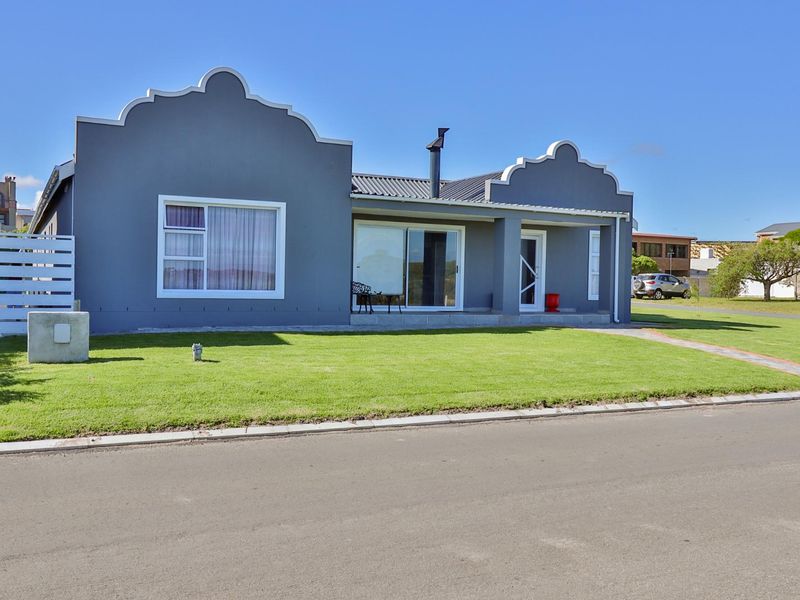 A well-maintained single-story home featuring a distinctive gabled parapet facade, metal roofing, and a neat front lawn with a paved walkway.