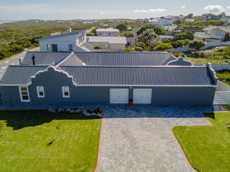 Aerial view of a modern house featuring a dark grey corrugated metal roof, gabled parapet walls, a double garage, and a paved driveway.