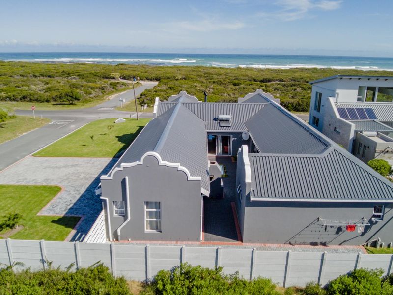 Aerial view of a modern coastal home featuring a grey metal roof, solar water heating, and a secure perimeter wall near the ocean.