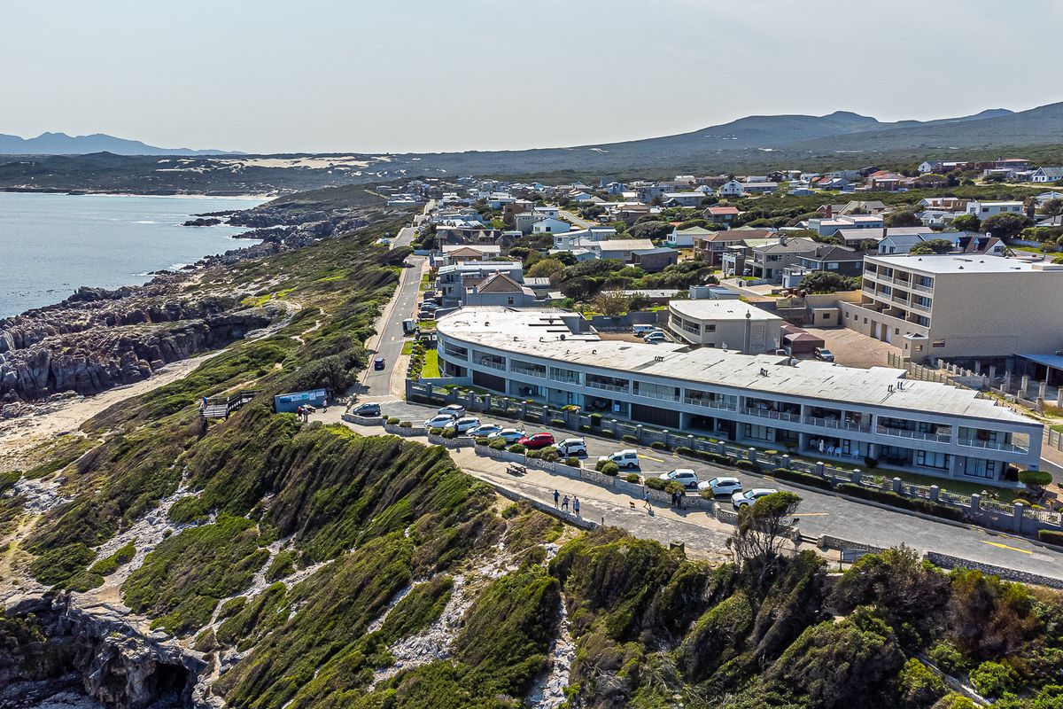 Aerial view of a coastal apartment complex situated on a cliffside, featuring ample parking and proximity to the ocean and local residential area.