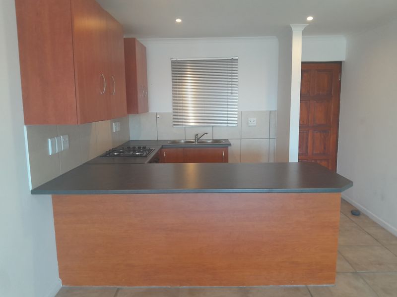 A functional kitchen featuring laminate cabinetry, a gas hob, double bowl sink, tiled backsplash, and a breakfast counter, presented in a clean, empty state.