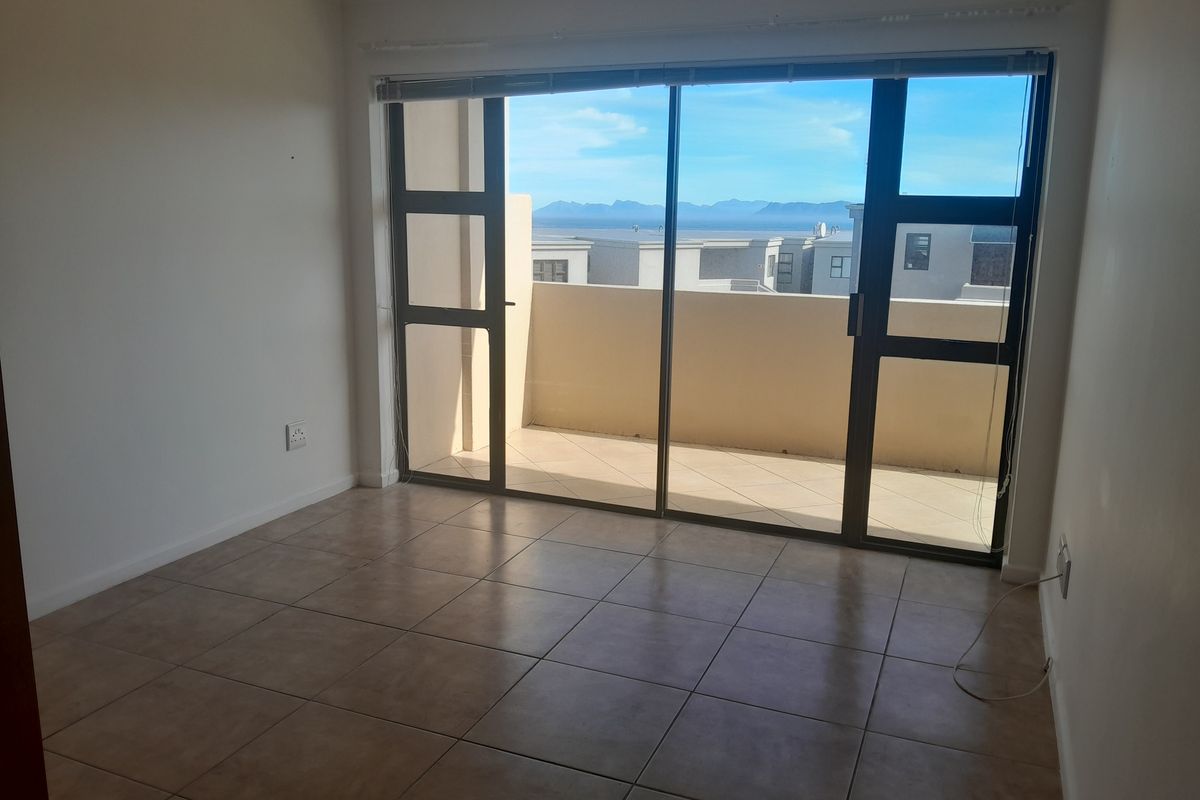 An empty bedroom featuring tiled flooring and large sliding glass doors that open onto a balcony with scenic mountain and coastal views.