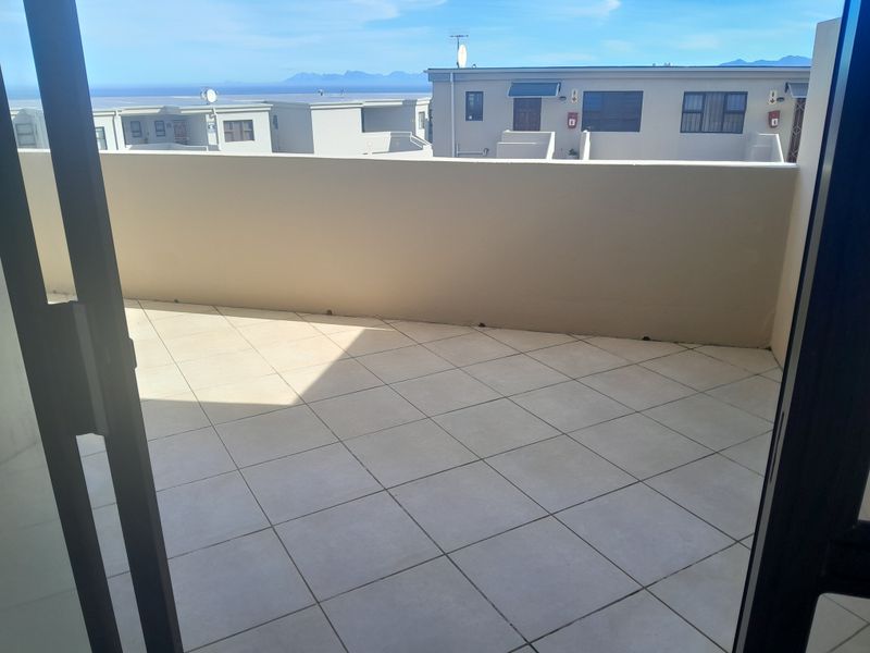 A spacious, open-air balcony featuring tiled flooring and a solid masonry balustrade, offering clear views of the surrounding residential complex and distant mountains.