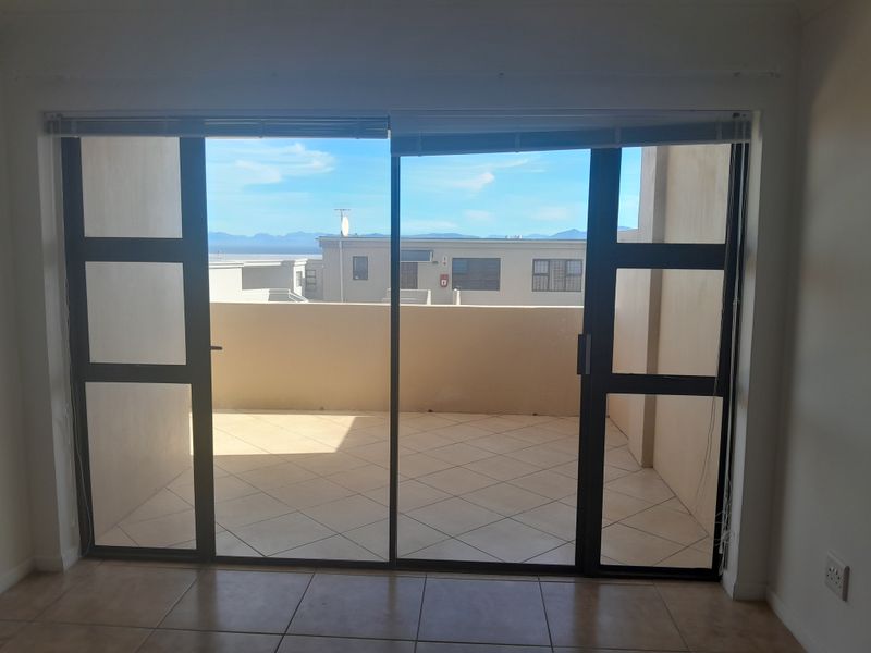 An empty living room featuring large sliding glass doors that open onto a tiled balcony with neighborhood and mountain views.