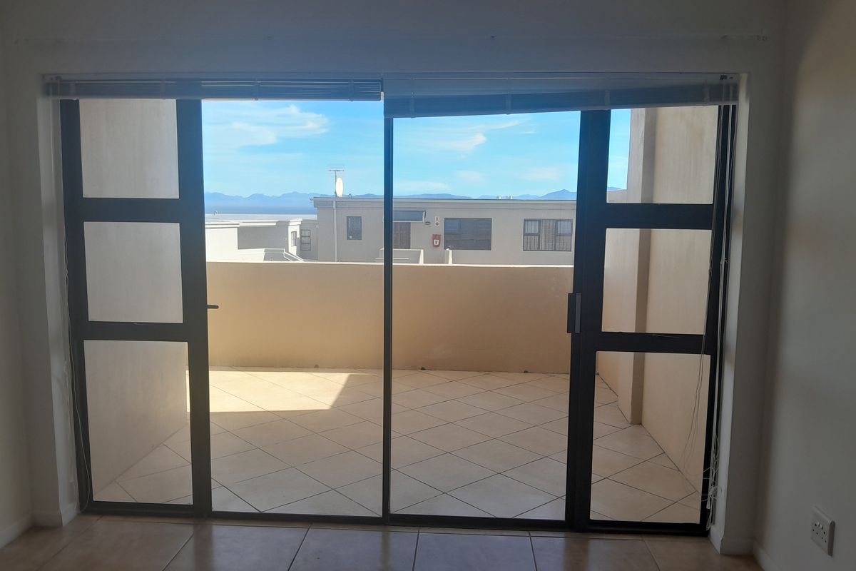An empty living room featuring large sliding glass doors that open onto a tiled balcony with neighborhood and mountain views.