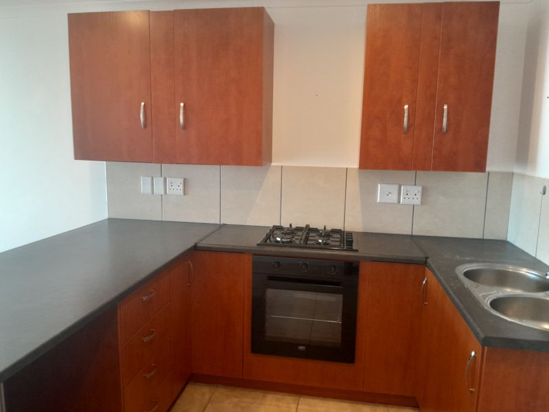 A functional kitchen featuring wooden cabinetry, dark laminate countertops, a built-in oven with gas hob, and a double bowl sink.