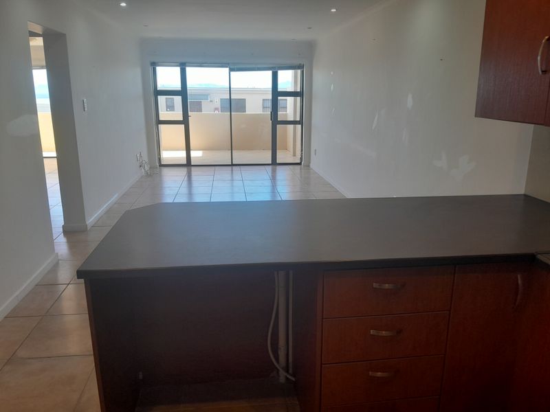 An open-plan living and kitchen area featuring tiled flooring, wooden cabinetry, and large sliding doors leading to an outdoor balcony space.