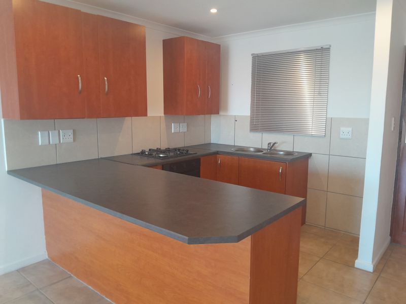 A functional kitchen featuring wood-finish cabinetry, dark laminate countertops, a gas hob, built-in oven, and a double sink with tiled backsplash.