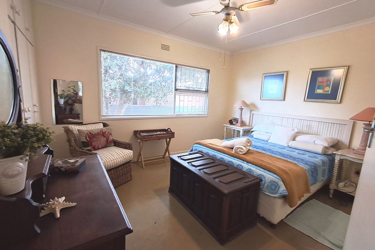 A functional bedroom featuring a ceiling fan, built-in wardrobe, and large window providing natural light.