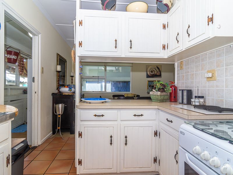 A functional kitchen featuring white cabinetry, laminate countertops, and tiled backsplash, with a view through to an adjacent living area.