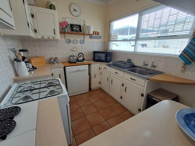 A functional kitchen featuring white cabinetry, tiled splashbacks, gas cooktop, and stainless steel sink with ample counter space and natural light.