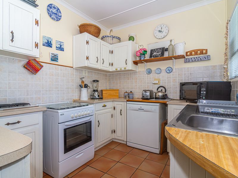 A functional kitchen featuring white cabinetry, tiled backsplash, tiled flooring, and a freestanding stove with integrated dishwasher space.