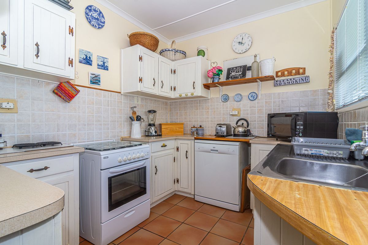 A functional kitchen featuring white cabinetry, tiled backsplash, tiled flooring, and a freestanding stove with integrated dishwasher space.