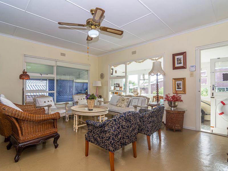 A bright living room featuring a ceiling fan, large windows providing natural light, and direct access to an adjoining space.